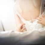 Seamstress helping future bride put on wedding dress after alterations